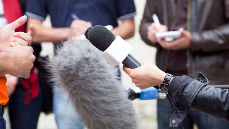 Journalisten umringen eine Person, viele schrieben, eine Person hält ein Mikrofon: Das SWR2 Archivradio sucht Audiobeiträge (Radio oder Podcast) aus dem Jahr 2021, die Radiogeschichte schreiben werden. (Foto: Colourbox)