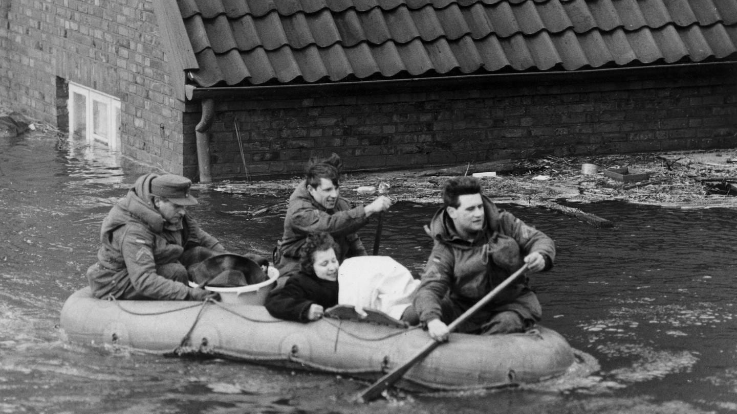 Eine Frau wird während der Sturmflut am 17. Februar 1962 mit einem Schlauchboot in Sicherheit gebracht. Das Wasser reicht fast bis zum Dach des Backsteinhauses im Hintergrund (Foto: picture-alliance / Reportdienste, picture-alliance / Gerd Herold | Gerd Herold)