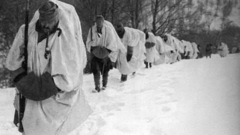 Soldaten in Schneemänteln laufen in einer Reihe, schneebedeckte Landschaft an der Seite. (Foto: SZ photo - Scherl)