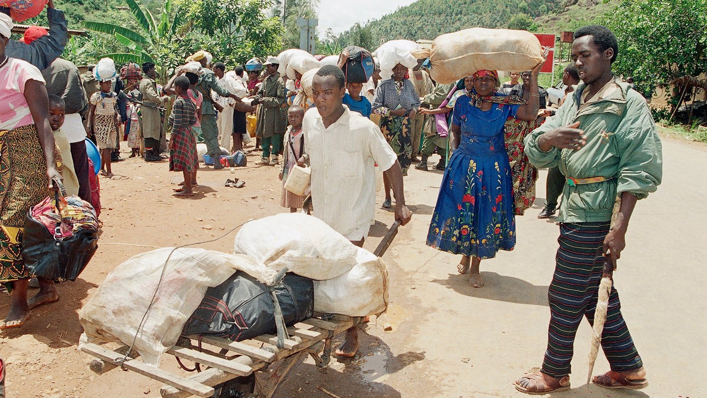 12. April 1994: Angehörige der Hutu fliehen südlich von Kigali vor den schweren Kämpfen zwischen den Regierungstruppen der Hutu und den Rebellen der Rwanda Patriotic Front (RPF) der Tutsi. Der Mann rechts ist Zivilist, Hutu und arbeitet auf der Seite der Regierungstruppen. Er kontrolliert die Flüchtlinge um sicherzustellen, dass keine Tutsi darunter sind. Hunderttausende Menschen fliehen nach dem Mord am Präsidenten Ruandas am 6. April 1994 vor den Massakern in Kagali und Umgebung. (Foto: picture-alliance / Reportdienste, picture alliance / ASSOCIATED PRESS | Jean-March Bouju)