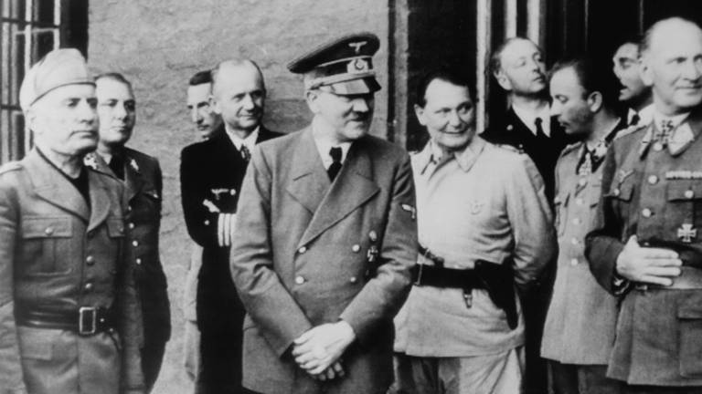 Adolf Hitler, der nach dem gescheiterten Attentat vom 20. Juli 1944 einen Verband an der linken Hand trägt. Von links:  Mussolini, Martin Borman, unbekannt, Adm. Dönitz, Hitler, Göring, Hermann Fegelein und Bruno Loerzer