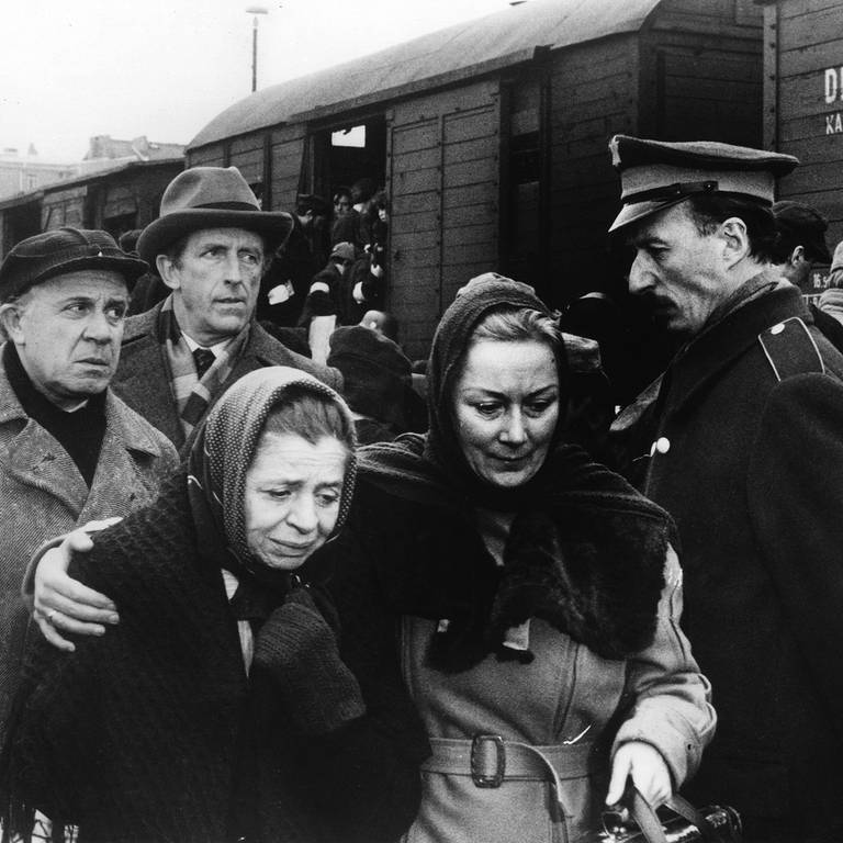 Filmszene Fernsehserie "Holocaust": Zwei Frauen in einer Menschenmenge halten sich im Arm, im Hintergrund ein Güterzug mit Menschen gefüllt