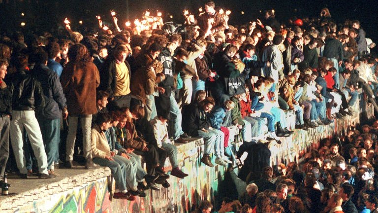 Jubelnde Menschen sitzen am 11.11.1989 mit Wunderkerzen auf der Berliner Mauer