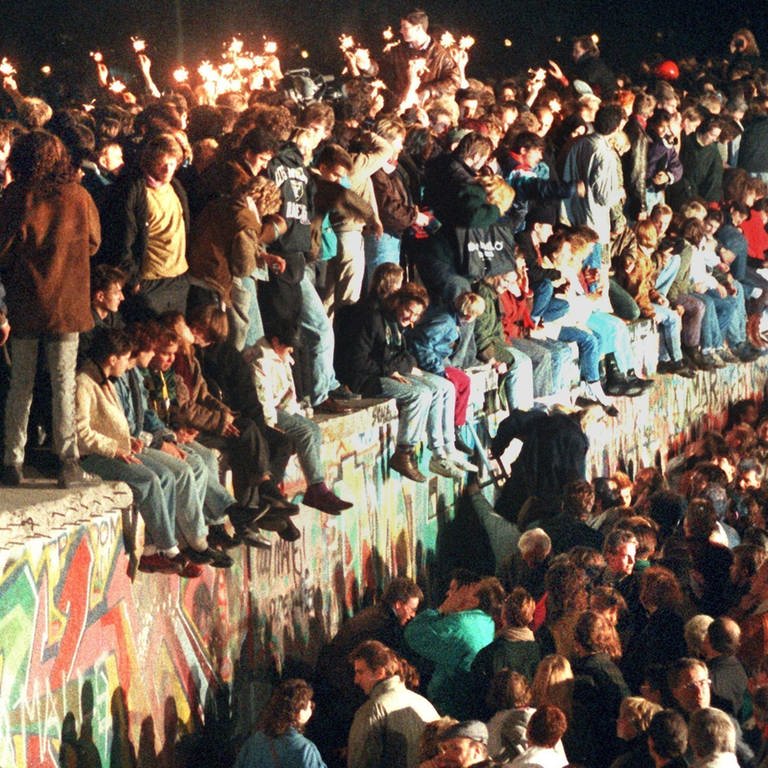 Jubelnde Menschen sitzen am 11.11.1989 mit Wunderkerzen auf der Berliner Mauer