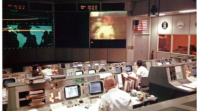 Gene Kranz (im Vordergrund mit dem Rücken zur Kamera), ein Flugdirektor von Apollo 13, beobachtet den Apollo-13-Astronauten und Piloten der Mondlandefähre Fred Haise während der vierten Fernsehübertragung der Mission am Abend des 13. April 1970 auf dem Bildschirm im Mission Operations Control Room. Kurz Nach der Übertragung ereignete sich eine Explosion, die jede Hoffnung auf eine Mondlandung zunichte machte und das Leben der Besatzung gefährdete.