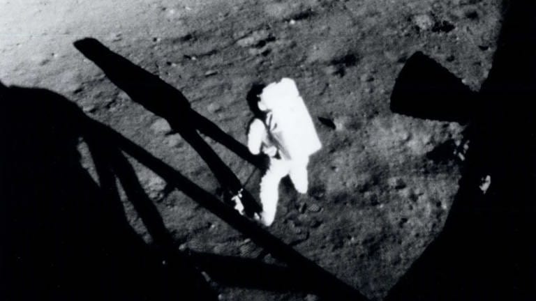 Der Kommandant von Apollo 11, Neil Armstrong, sammelt Proben des Mondbodens, kurz nachdem er am 20. Juli 1969 seinen historischen ersten Schritt auf der Oberfläche des Mondes gemacht hat. Das Foto wurde von Edwin "Buzz" Aldrin aus dem Inneren des Landefahrzeugs aufgenommen. Im Vordergrund ist ein Teil des Fahrzeugschattens sichtbar.