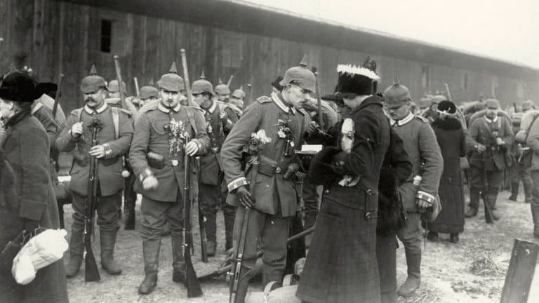 Ein Soldat nimmt Abschied von seiner Frau oder Freundin, im Hintergrund weitere Soldaten: Abschiedsszene vor der Abfahrt eines Reservistentransports auf einem Berliner Güterbahnhofim Winter 1914.