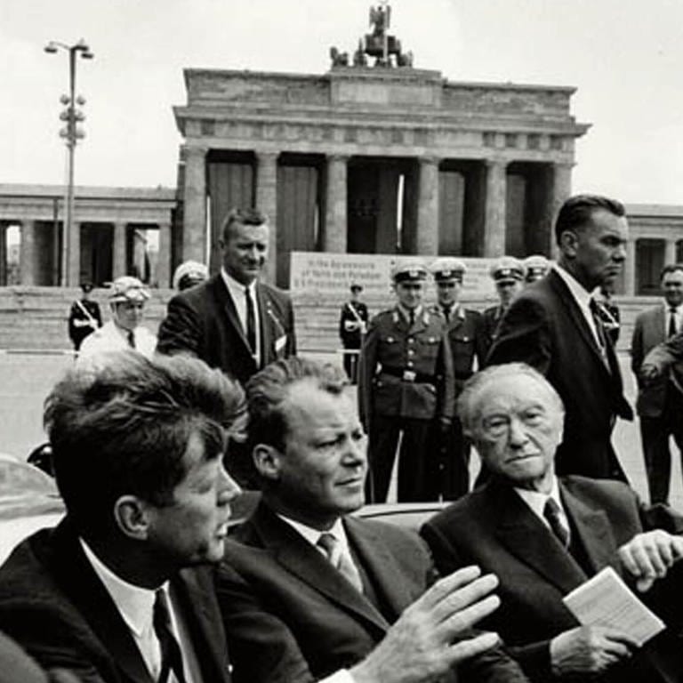 Präsident John F. Kennedy (links), Willy Brandt (Mitte; Bürgermeister von West-Berlin) und Bundeskanzler Konrad Adenauer am 26. Juni 1963 in einem Auto am Brandenburger Tor