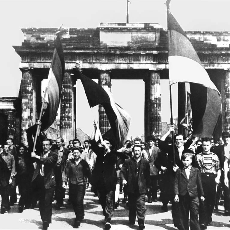 Ost-Berliner marschieren am 17 Juni 1953 mit wehenden Fahnen vom Ost-Sektor aus durch das Brandenburger Tor. Nach Streiks in Ost-Berlin kam es zum Volksaufstand, der von sowjetischen Truppen niedergeschlagen wurde. (Foto: picture-alliance / Reportdienste, picture-alliance / dpa | UPI)