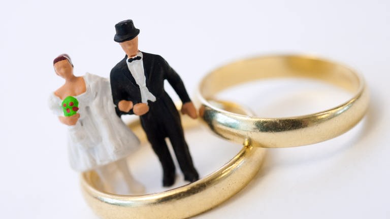 Figur eines Brautpaars in einem von zwei goldenen Eheringen: 