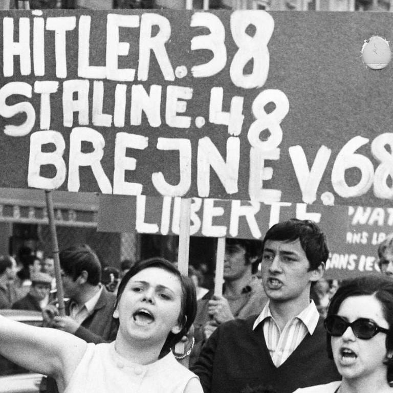 Menschen demonstrieren am 22. August 1968 in Prag gegen die Besetzung der Tschechoslowakei durch die Sowjetunion. Auf einem Plakat steht: "Hitler 38, Stalin 48, Brejnev 68"