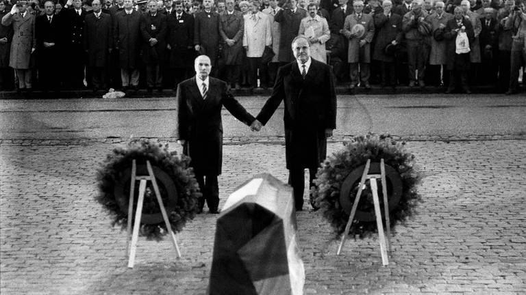 Helmut Kohl und François Mitterrand Hände haltend während der Feierstunde zum Gedenken an die Gefallenen beider Weltkriege in Verdun