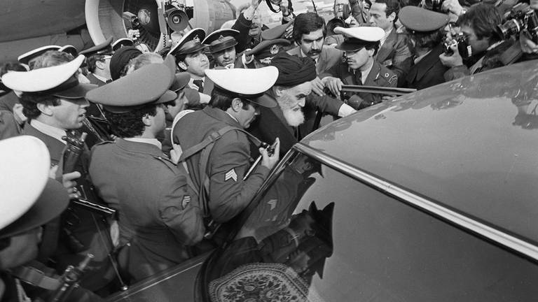 Ajatollah Khomeini wird stark bedrängt, als er am 1.2.1979 aus dem Pariser Exil in den Iran zurückkehrt. Sicherheitsleute schützen ihn, als er am Flughafen Teheran in ein Auto steigt. (Foto: picture-alliance / Reportdienste, picture alliance / ASSOCIATED PRESS | uncredited)