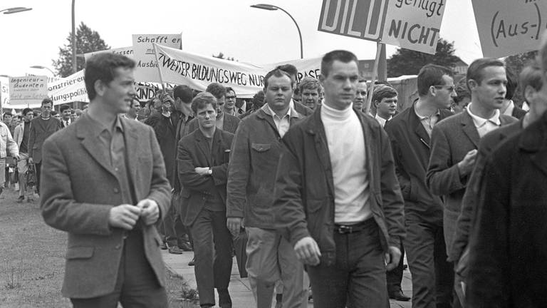 Als Folge eines weiterhin sinkenden Ausbildungsniveaus an den Universitäten demonstrierten rund 1.500 Studenten am 30.6.1967 in Hamburg für ein Bildungsförderungsgesetz. Auf ihrem Weg zur "Meckerwiese" trugen die Studenten zahlreiche Schilder und Plakate mit ihren Forderungen.