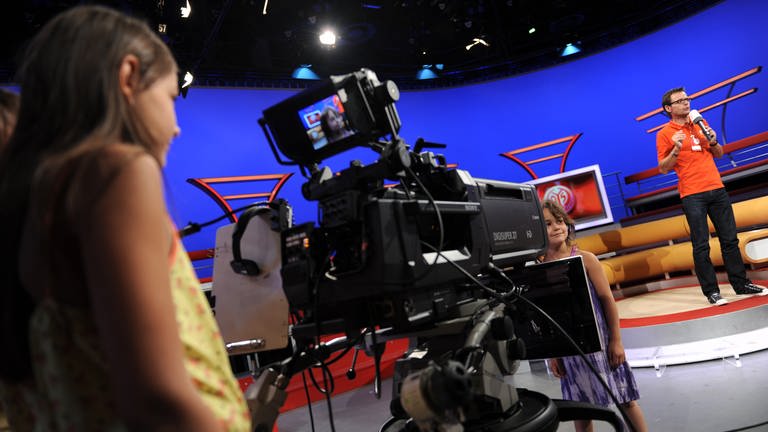 Ein Mädchen steht im Flutlicht-Fernsehstudio vor einer Kamera