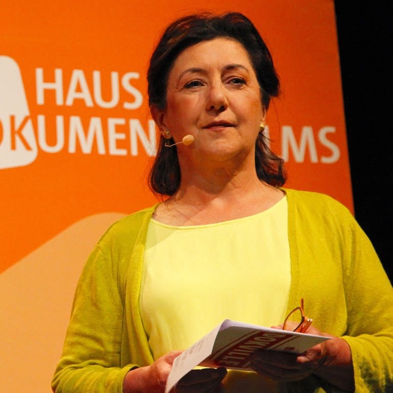 Die Geschäftsführerin im Haus des Dokumentarfilms, Ulrike Becker, steht vor einer Logowand und trägt ein Mikrofon