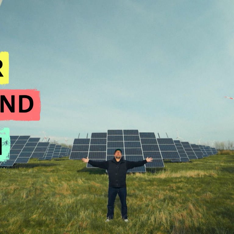 Bjarne Mädel steht mit ausgebreiteten Armen vor einem Solarpark