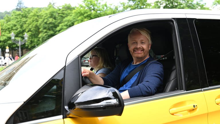 Ross Antony auf dem Fahrersitz des "Down the Road"-Tourbusses, neben ihm sitzt Angela (Foto: SWR, SEO Entertainment/Ben Pakalski)