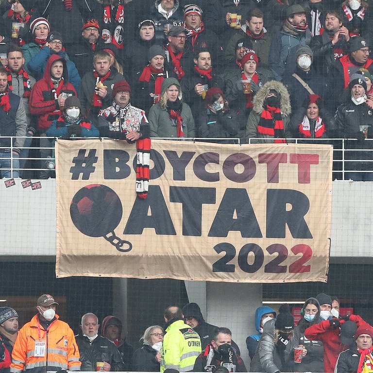 Menschen auf einer Fußballtribüne, am Geländer ein Transparent, auf dem "Boykott Qatar 2022" steht.