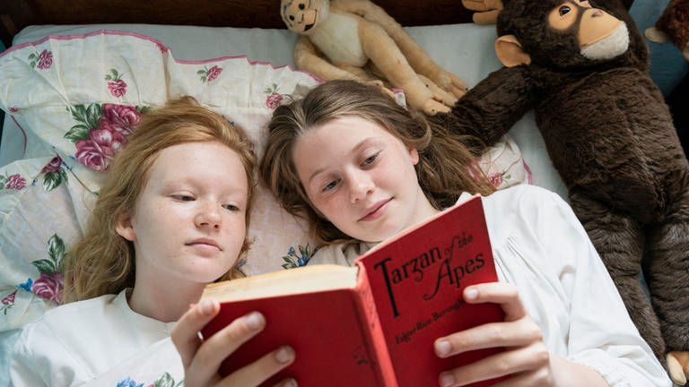 Jane (Aurelia Ott, re.) und ihre Freundin Sally (Lilli Falk, li.) liegen gemeinsam im Bett und lesen "Tarzan of the Apes". 