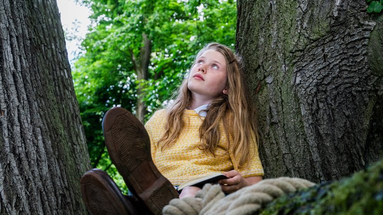 Jane (Aurelia Ott) sitzt grübelnd auf einem Baum. 