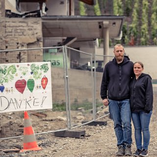 Familie Krämer steht vor dem zerstörten Haus, ein Plakat mit der Aufschrift "Danke" hängt am Saun. (Foto: SWR)