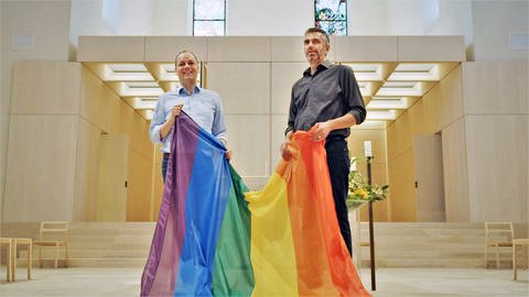 Liebe ohne Segen? Heiko und Marius mit einer Regenbogenfahne in der Kirche (Foto: SWR)