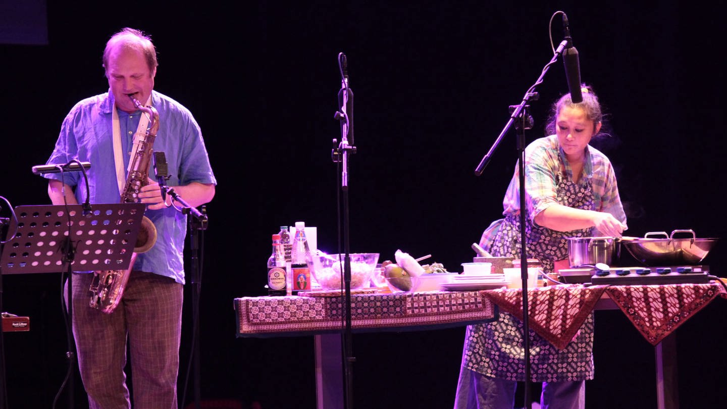 Tobias Delius Sextett spielt, während Ciska Jansen (re.) auf der Bühne ein indonesisches Reisgericht zubereitet.