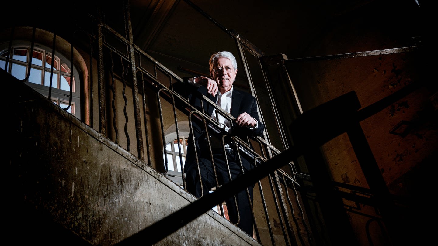Frank Elstner steht in einem Treppenhaus, lehnt am Geländer und blickt nach unten. (Foto: SWR)