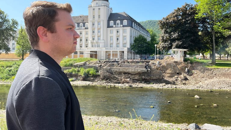 Reporter Marius Reichert ist Host des Podcasts "Die Flut - Warum musste Johanna sterben". Er steht am Ufer der Ahr, gegenüber dem zerstörten Kurhaus in Bad Neuenahr-Ahrweiler. (Foto: SWR)