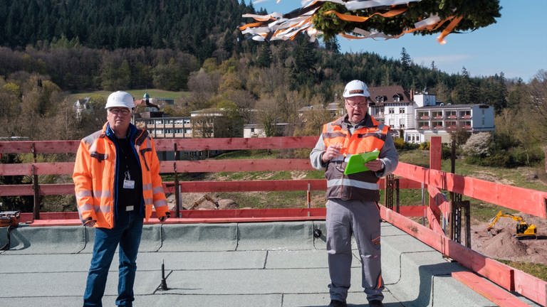 Zwei Herren in Helmen und in orangenen Sicherheitsjacken auf einer Baustelle (Foto: SWR)