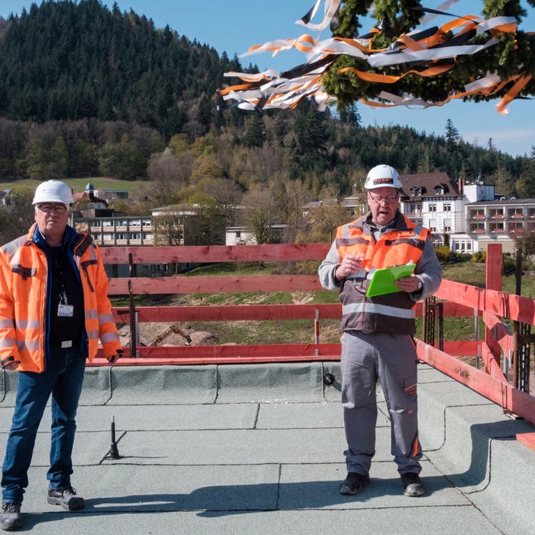 Zwei Herren in Helmen und in orangenen Sicherheitsjacken auf einer Baustelle