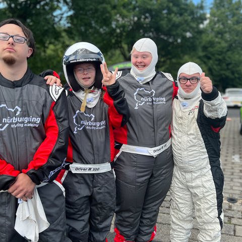 Ein Teil der Gruppe steht in Vollmontur vor einem Rennauto am Nürburgring (v.l.n.r. Jonas, Rosalie, Angela, Patrick) (Foto: SWR, SEO)