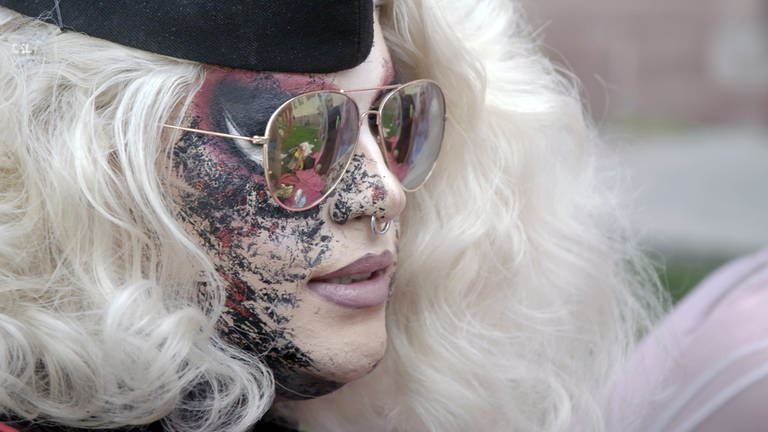 Dragqueen Macy M. Meyers im Profilfoto. Sie trägt einen platinblonde Perücke, aufwändiges Make-up und eine goldgerahmte Sonnenbrille. Sie hat einen Nasenring. (Foto: SWR)
