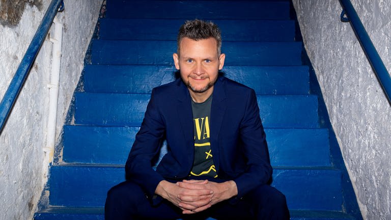 Tobias Mann, Kabarettist und Musiker. Auf einer blauen Treppe sitzend. (Foto: SWR, Thomas Klose )