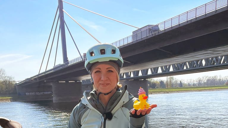 Anna Lena Dörr mit der Jubiläumsente, dem "Staffelstab" der Rheinradwanderung. Sie steht an der Rheinbrücke Maxau zwischen Karlsruhe und Wörth. (Foto: SWR, Rolf Stephan)