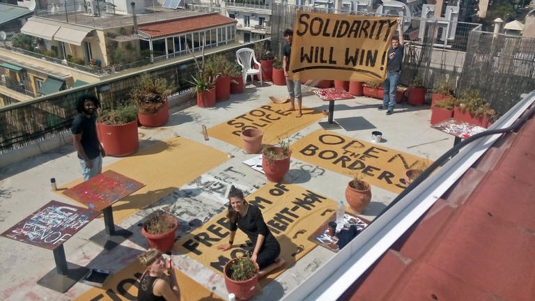 „#widerstand“: Protagonistin Helene und andere Aktivisten malen Banner auf dem Dach vom besetzten Hotel City Plaza in Athen. Die Regisseurin Britta Schoening ist zur Recherche anwesend. © SWRBritta Schoening 