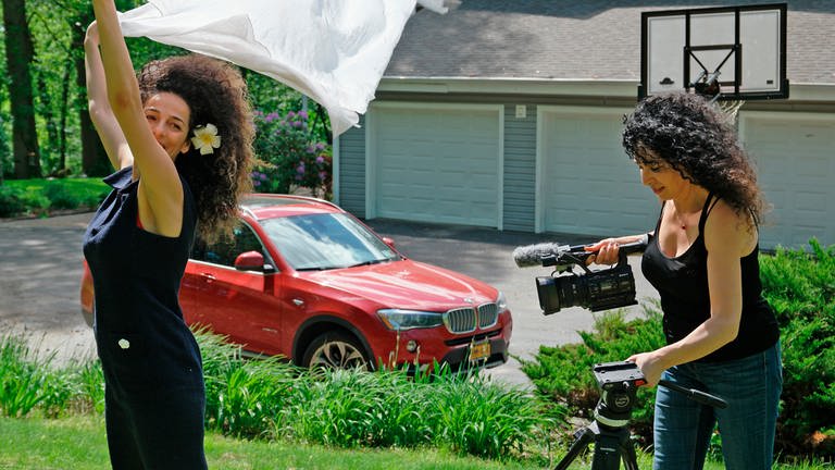 Naahid filmt Masih in ihrem Garten, im Hintergrund ist ein graues Haus, davor ein roter BMW zu sehen