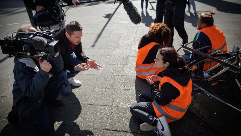 ARD Story: Radikal fürs Klima - Helden oder Kriminelle? Aktivisten der "Letzten Generation" werden bei einer Straßenblockade auf dem Kurfürstendamm in Berlin interviewt. (Foto: SWR, © SWR/Gordon Welters)
