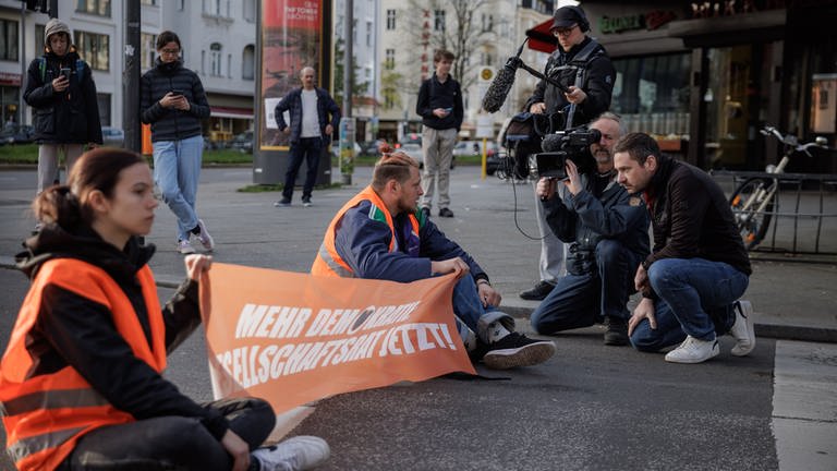 ARD Story: Radikal fürs Klima - Helden oder Kriminelle? Aktivisten der "Letzten Generation" werden bei einer Straßenblockade auf dem Kurfürstendamm in Berlin interviewt. (Foto: SWR, © SWR/Gordon Welters)