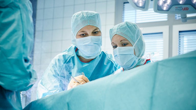 Zwei Ärztinnen in OP-Kleidung beugen sich im Operationssaal über eine abgedeckte Person. "SOS Großstadtklinik" in der ARD Mediathek. (Foto: SWR, Volker Schrank)