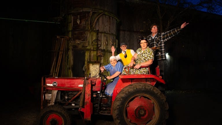 Comedy Duos Hillu's Herzdropfa (Hillu Stoll, li. und Franz Auber) und Elsbeth und Alois Gscheidle (Birgit Pfeiffer und Marcus Neuweiler, re.) sitzen auf einem roten Traktor