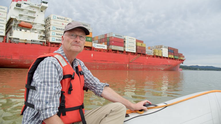 Sven Plöger auf einem kleinen Schlauchboot, dahinter ein großes Container-Schiff. (Foto: SWR, Jonas Sichert)