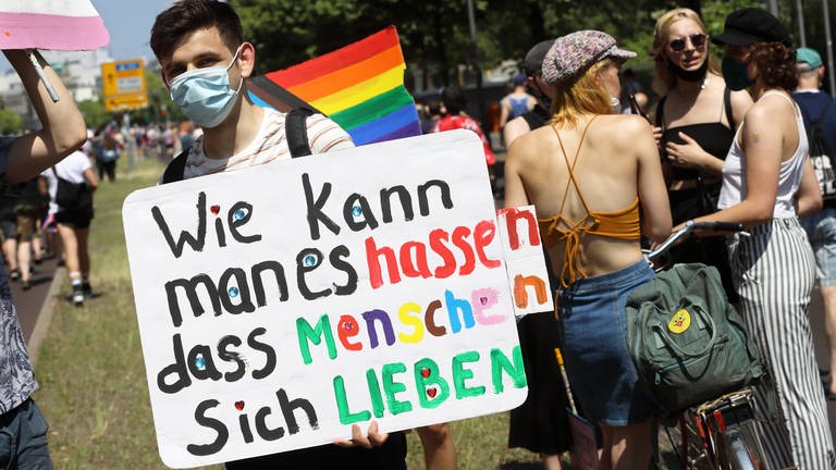 Junger Mann mit Plakat "Wie kann man es hassen dass Menschen sich lieben" (Foto: IMAGO, Müller-Stauffenberg)