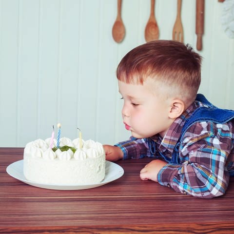 Ein Junge pustet Kerzen auf einer Geburtstagstorte aus (Foto: IMAGO, imago images / agefotostock)