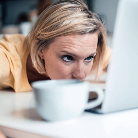 Frau liegt vor einem Laptop und schaut müde auf den Bildschirm: Wir brauchen mehr als ein Drittel unseres Gehirns, um unsere Augen zu bedienen. Wenn wir müde sind, ist unsere Sehrleistung deutlich geringer. (Foto: imago images, IMAGO / Westend61)