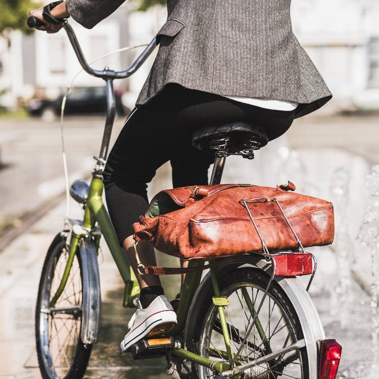 Radfahrerin mit Aktentasche auf dem Gepäckträger: Durch Radfahren kann man seine persönliche Klimabilanz verbessern (Foto: IMAGO, imago images / Westend61)