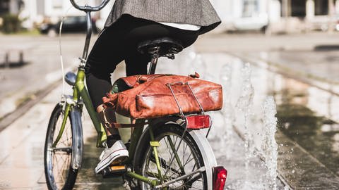 Radfahrerin mit Aktentasche auf dem Gepäckträger: Durch Radfahren kann man seine persönliche Klimabilanz verbessern (Foto: IMAGO, imago images / Westend61)