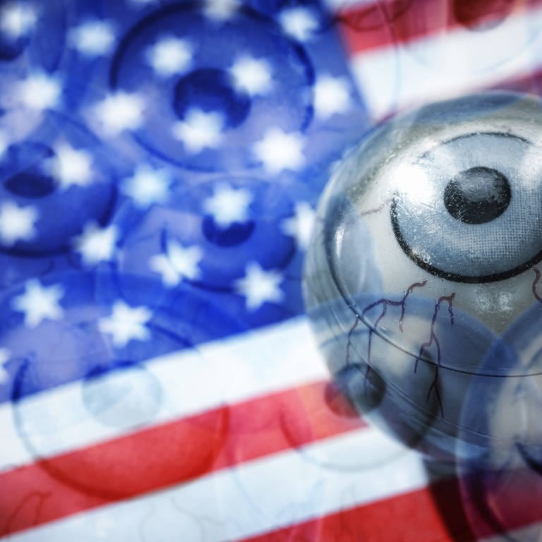 Amerikanische Flagge, darauf ein Auge (Grafik): Die USA spielen eine wichtige Rolle bei Verschwörungstheorien. Grund sind der weltweite Einfluss der USA und der amerikanischen Popkultur (Foto: IMAGO, IMAGO / Christian Ohde)