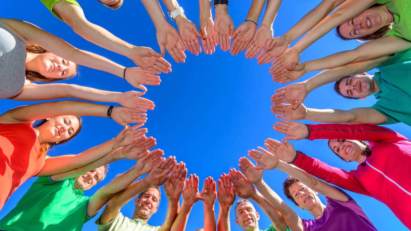 Viele Menschen stehen im Kreis und bilden mit ihren Händen einen inneren Kreis (Foto: IMAGO, IMAGO / Alexander Rochau)